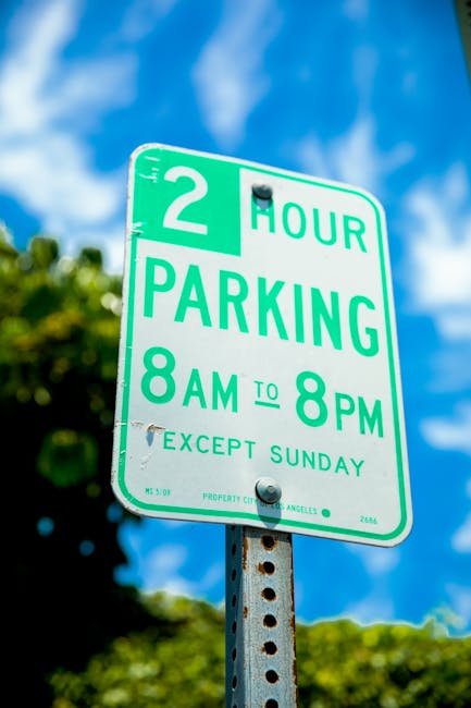 A close-up image of a green and white parking restriction sign mounted on a metal pole, with the background featuring a partly cloudy blue sky and blurred green foliage. The sign indicates a two-hour